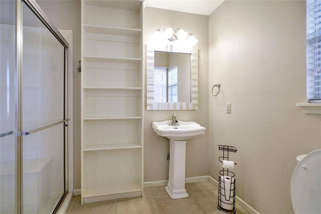 1114 Brookshire Drive, Tyler, TX 75071 Bathroom featuring a glass-enclosed shower with built-in bench, floor-to-ceiling shelving, pedestal sink, mirrored vanity with sconce lighting, and tiled flooring