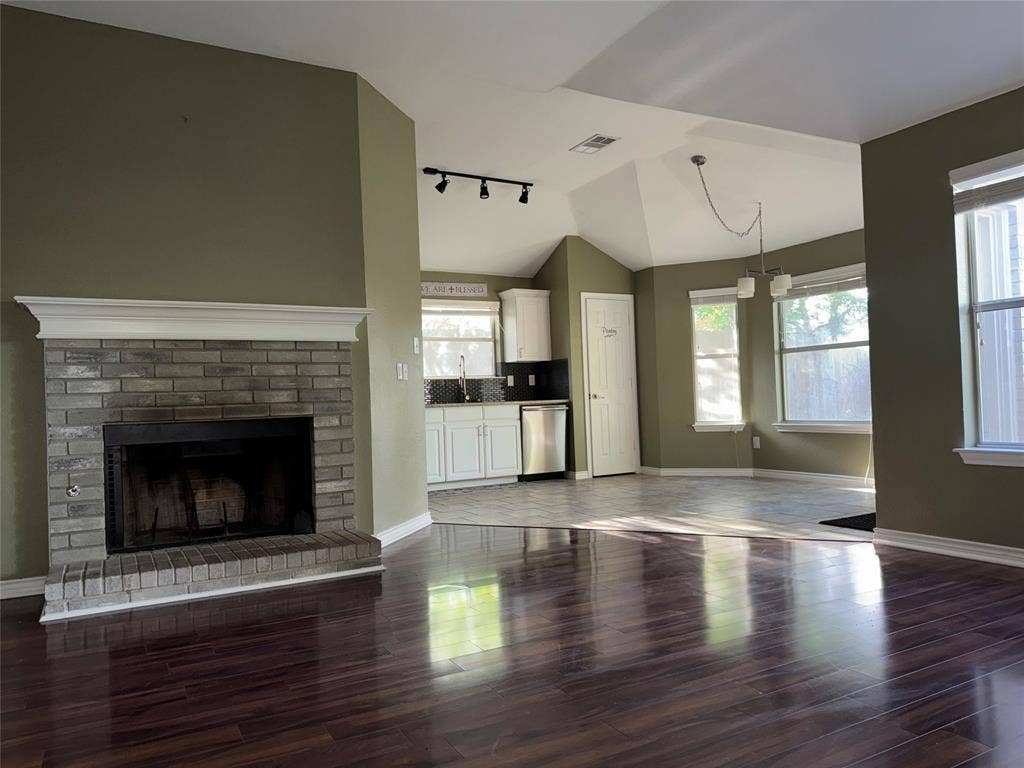 Living area featuring a brick fireplace with a white mantel, wood-finish flooring, and a vaulted ceiling