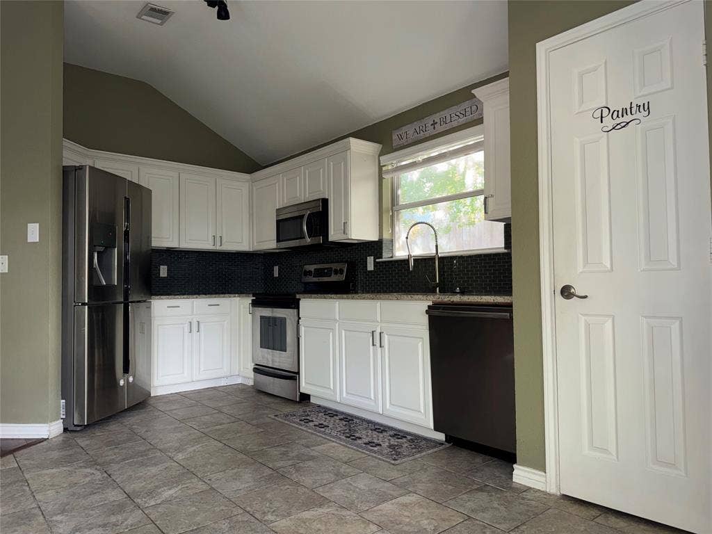 Kitchen featuring white cabinetry, dark tile backsplash, stainless steel appliances, and a vaulted ceiling