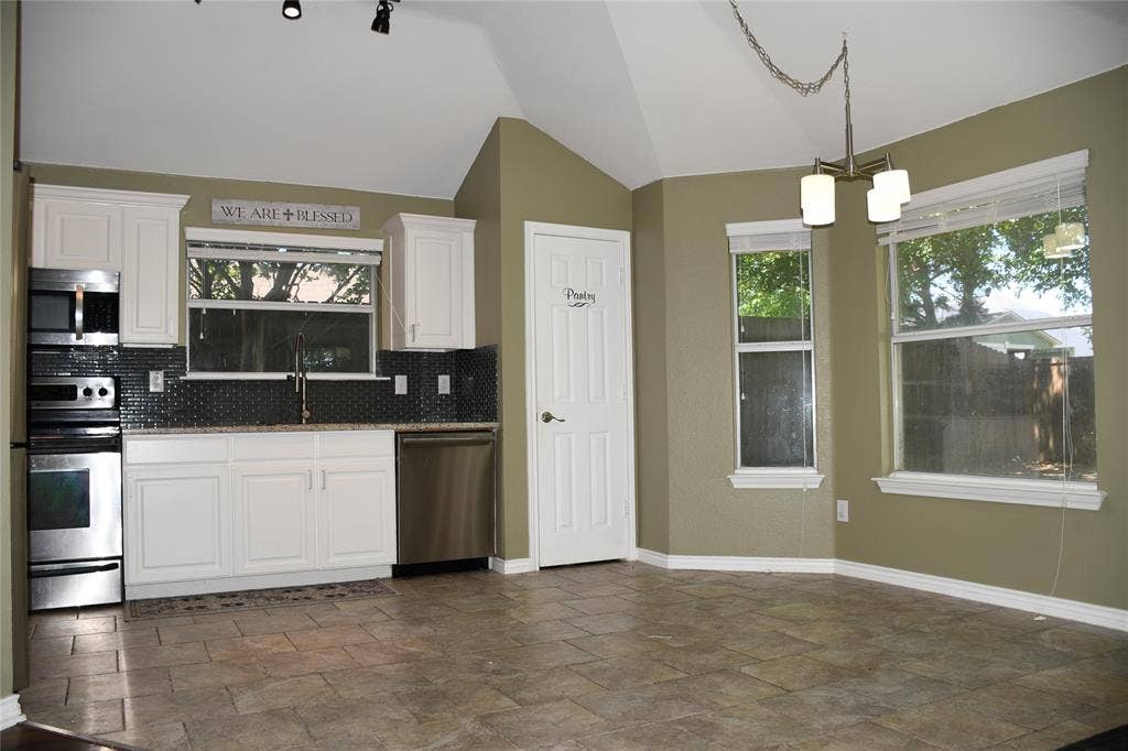 Kitchen area featuring white cabinetry, stainless steel appliances, dark tile backsplash, and a vaulted ceiling