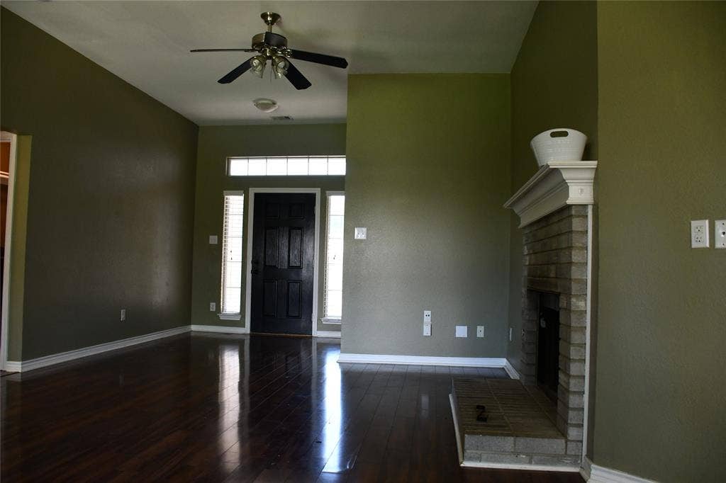Spacious interior featuring high ceilings, dark wood-finish flooring, a brick fireplace with a white mantel, and a dark paneled entry door with sidelight windows and transom