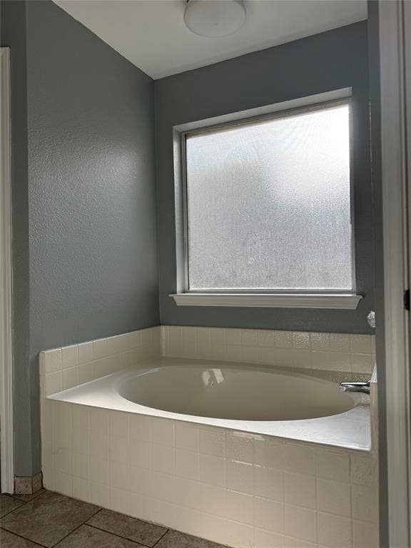 Recessed soaking tub with white tile surround, frosted window, and light gray painted walls