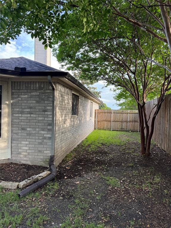 Private side yard featuring a partial brick exterior, mature trees, and wood fencing
