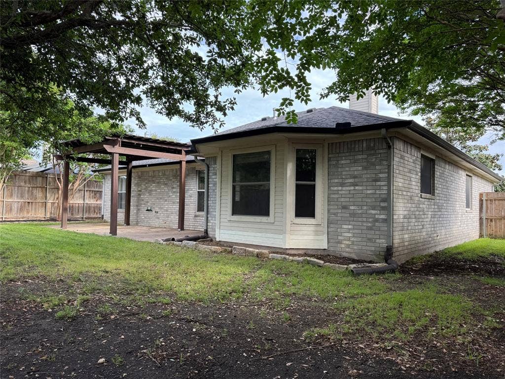 Expansive backyard featuring a pergola-covered patio, light brick exterior, bay window, dark shingle roof, and a wood privacy fence