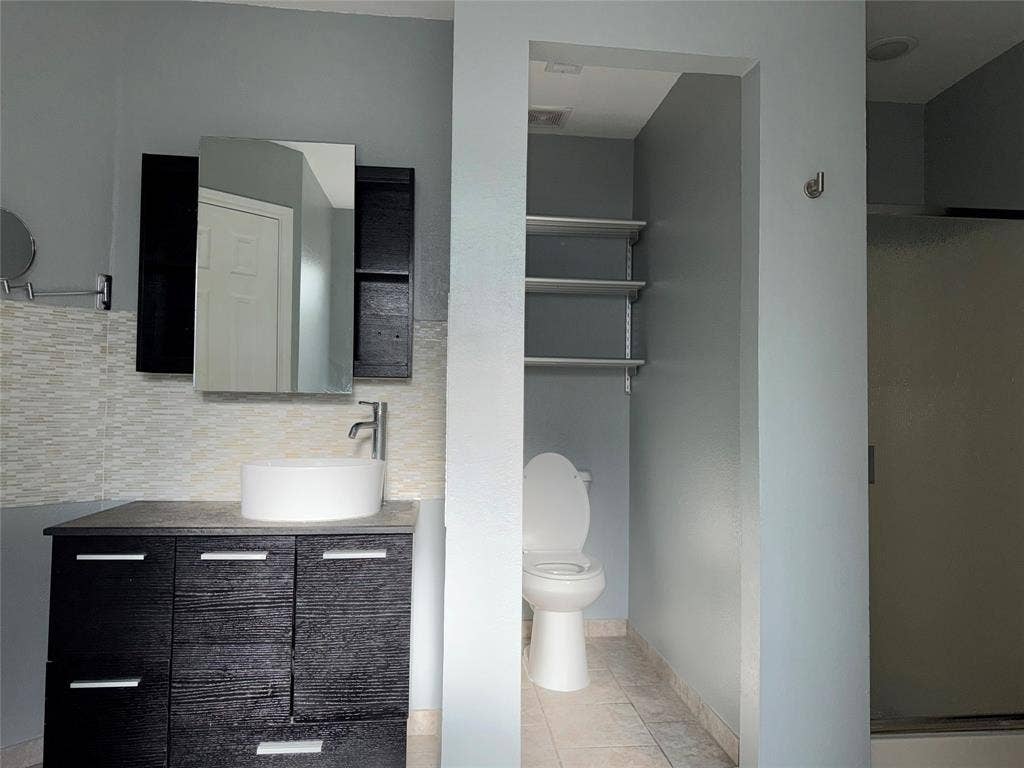 Bathroom featuring a contemporary dark wood-finish vanity with a white vessel sink, a chrome faucet, and a large mirrored medicine cabinet