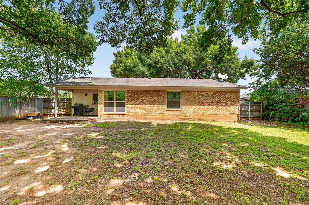 224 Hudson Avenue, Crowley, TX 76036 Spacious backyard with mature trees, brick exterior, covered patio, and privacy fencing