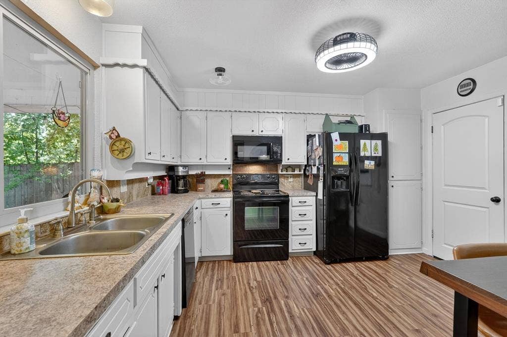 224 Hudson Avenue, Crowley, TX 76036 Kitchen featuring wood-finish flooring, white cabinetry, a double basin stainless steel sink, and black appliances