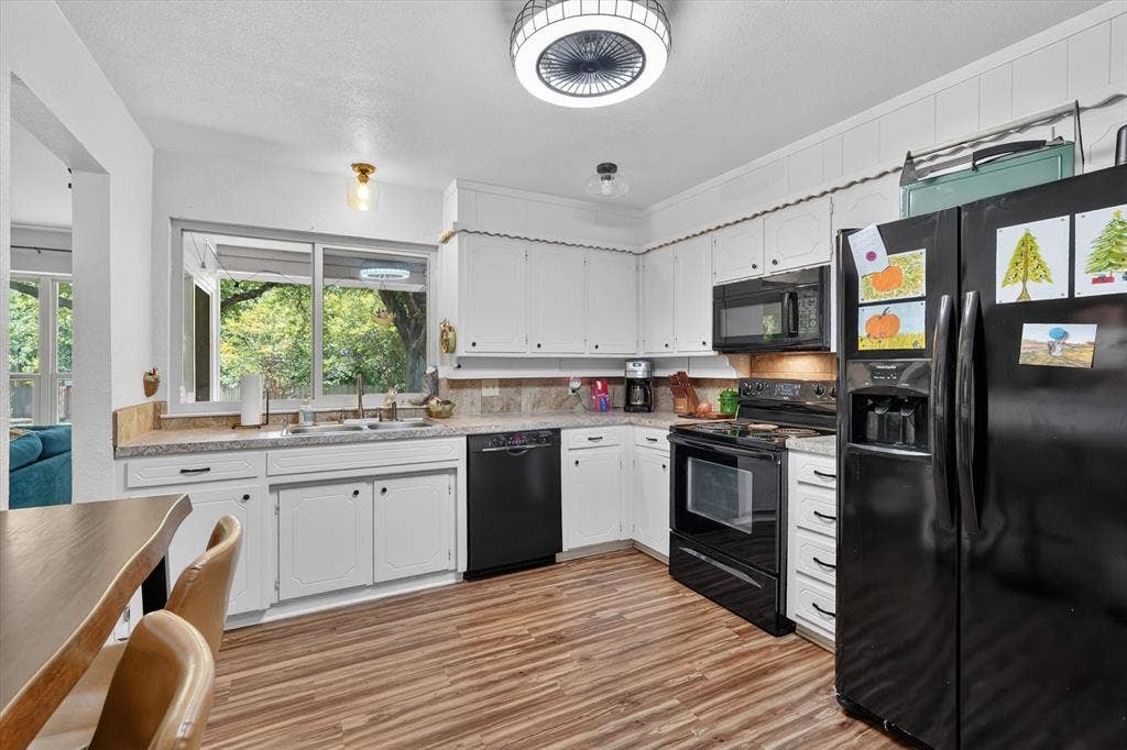 224 Hudson Avenue, Crowley, TX 76036 Kitchen featuring white cabinetry, wood-finish flooring, a stainless steel sink, black appliances, and a window above the sink