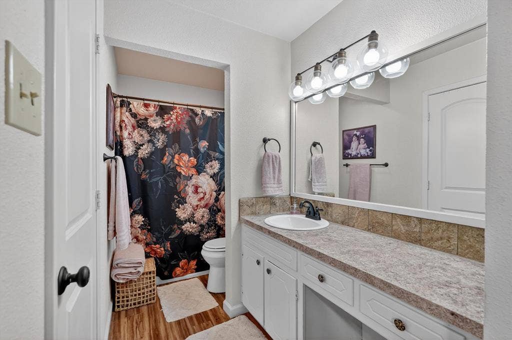 224 Hudson Avenue, Crowley, TX 76036 Well-lit bathroom featuring a single-sink vanity with a laminate countertop, a large mirror, a four-light fixture, and wood-finish flooring