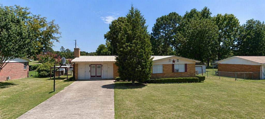 613 Laurel Road, Athens, TX 75751 Brick exterior with a metal roof, featuring a concrete driveway, established front lawn, and mature trees