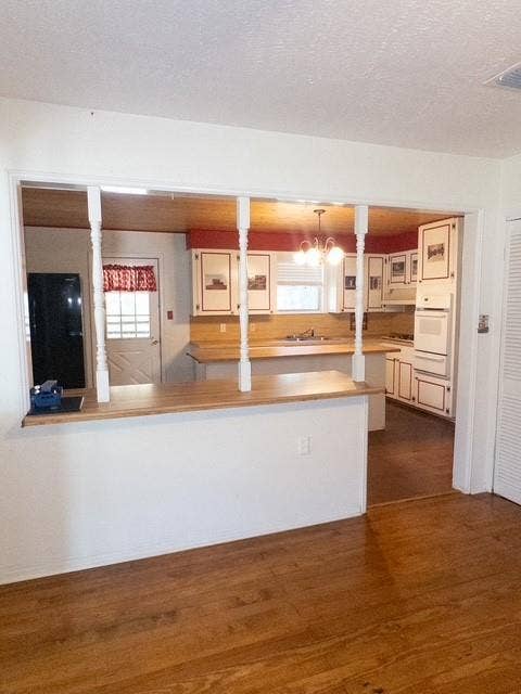 613 Laurel Road, Athens, TX 75751 Open concept kitchen with wood-finish flooring, white cabinetry, integrated appliances, and a pass-through bar with turned newel posts
