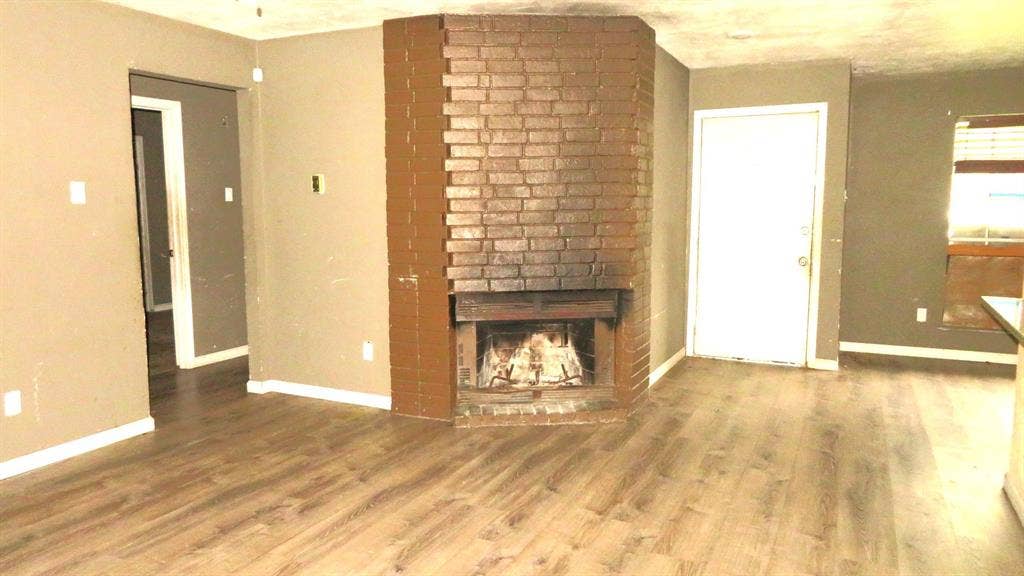 6525 Palm Island Street, Dallas, TX 75241 Corner brick fireplace with a raised hearth, wood-finish flooring, and neutral wall paint