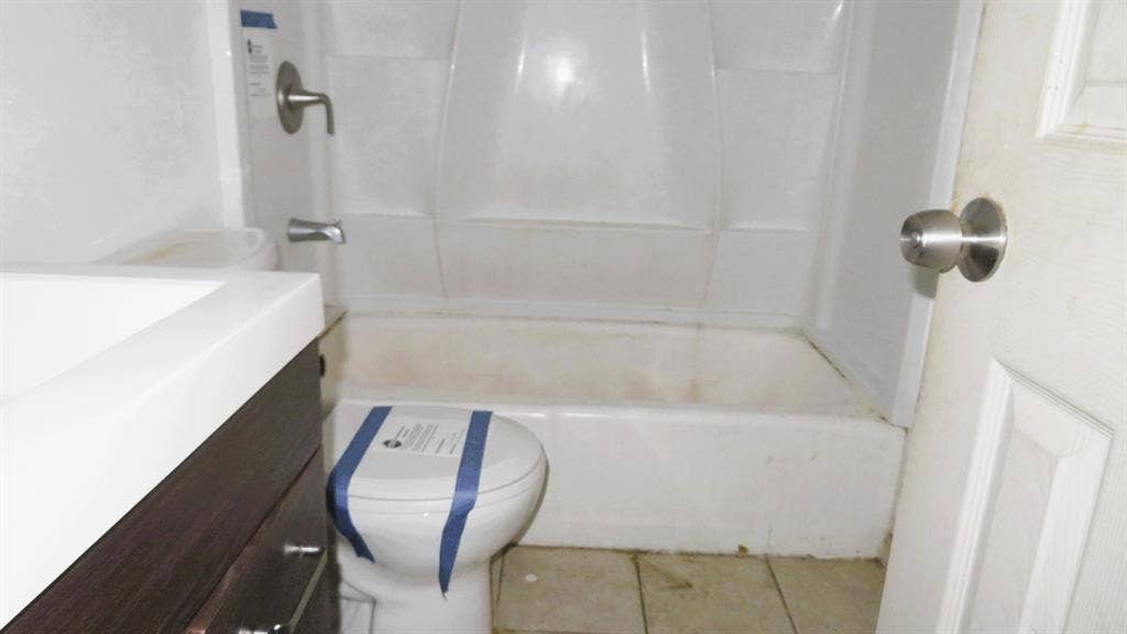 6525 Palm Island Street, Dallas, TX 75241 Bathroom featuring a white integrated sink and countertop, wood-finish vanity with hardware, white toilet, and a white shower-tub combination with a brushed nickel showerhead and faucet