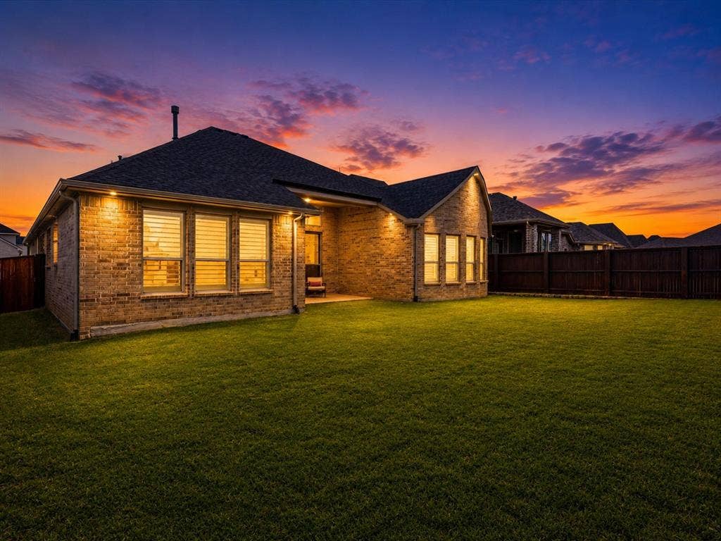 Expansive rear lawn featuring a brick exterior with multiple windows, a covered patio area, and a privacy fence