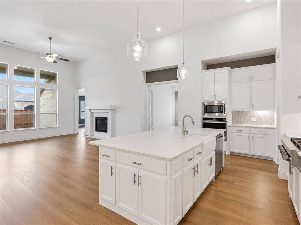 Open-concept kitchen featuring a large island with sink, white shaker cabinetry, stainless steel appliances, and pendant lighting. This image has been virtually enhanced for marketing purposes.