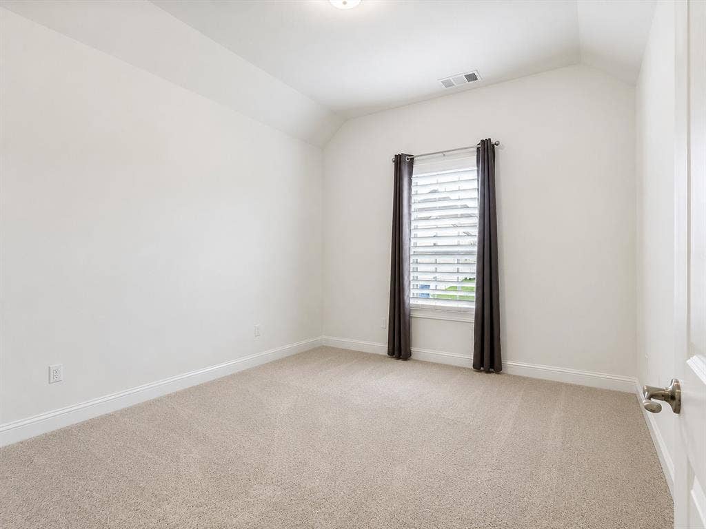 Carpeted interior space featuring neutral wall tones, baseboard molding, a window with horizontal blinds, and a vaulted ceiling