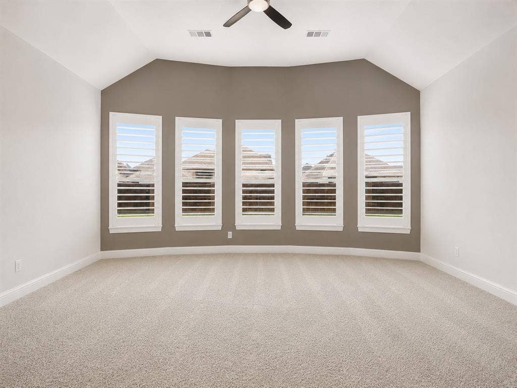 Vaulted ceiling with a ceiling fan, five windows with plantation shutters, neutral-toned walls, and carpet flooring