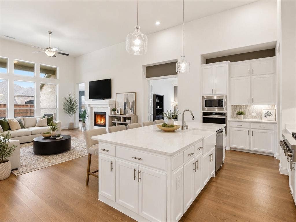 Open-concept living area featuring a kitchen island with seating, wood-finish flooring, a contemporary fireplace, high ceilings, and large windows. This image has been virtually enhanced for marketing purposes.