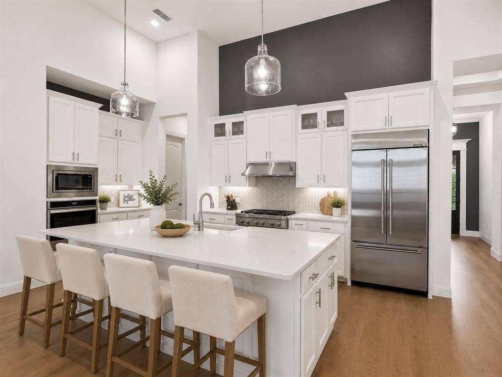 Kitchen featuring white cabinetry, stainless steel appliances, a large central island with seating, pendant lighting, and wood-finish flooring. This image has been virtually enhanced for marketing purposes.