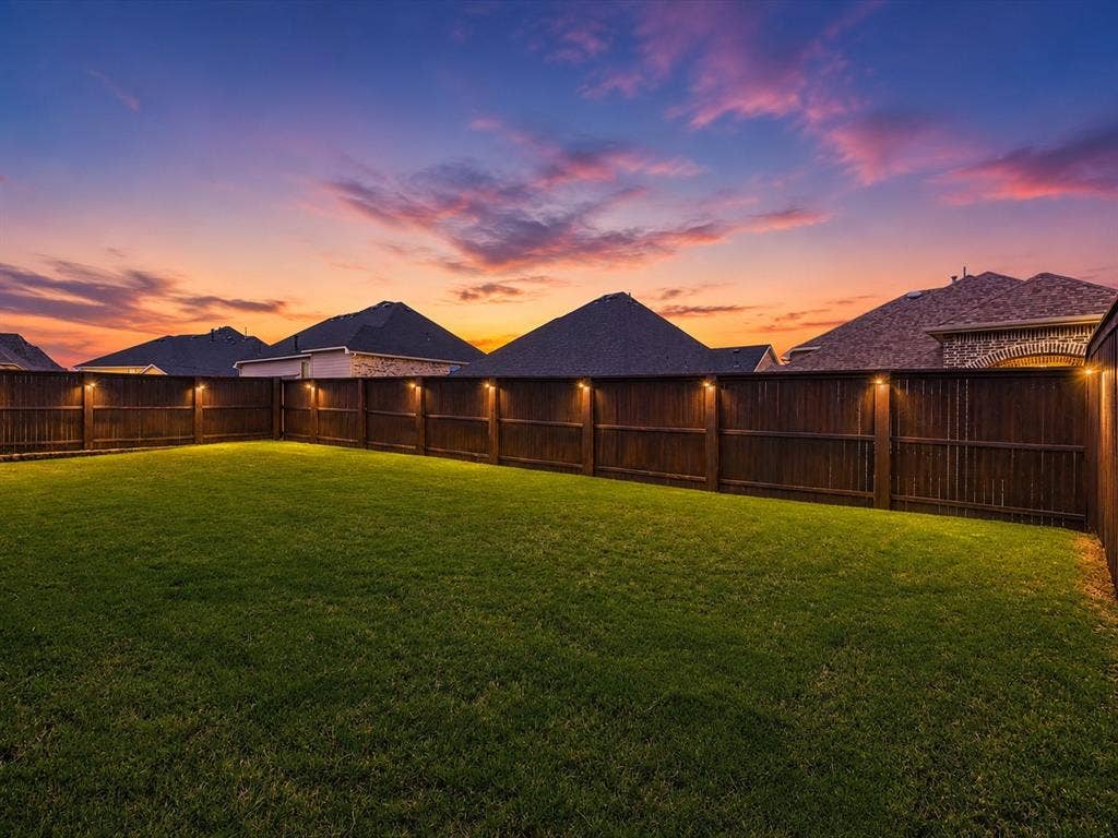 Expansive backyard featuring a lush green lawn, full wood privacy fencing, and integrated fence lighting