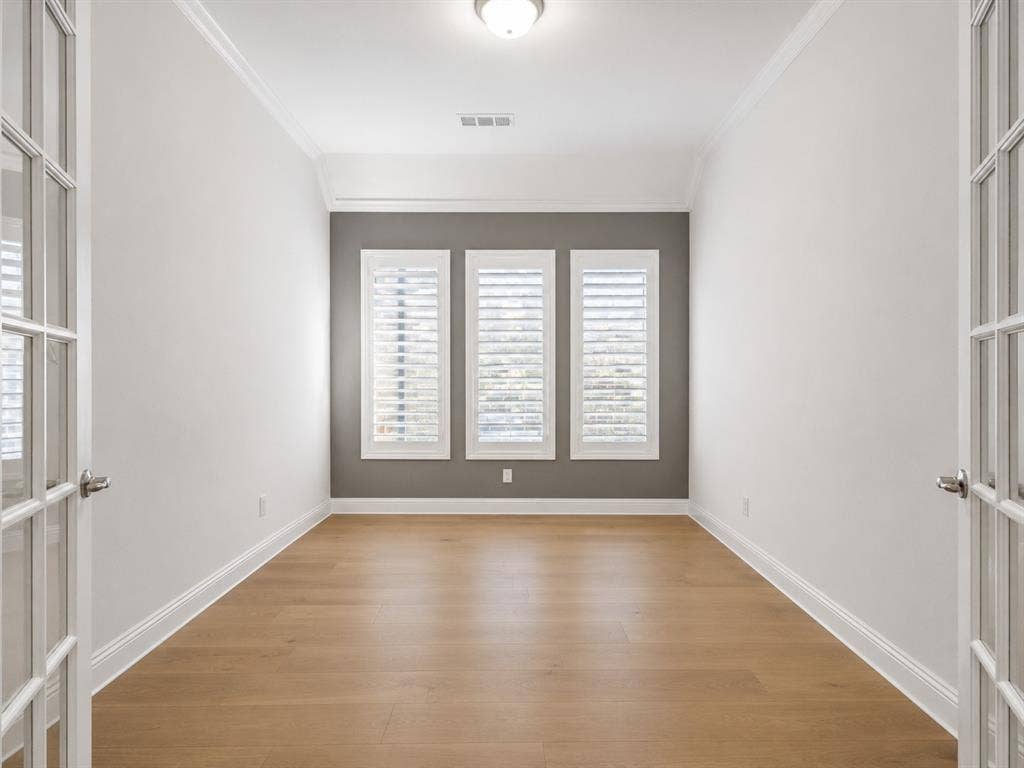 Room featuring wood-finish flooring, white baseboards, and white crown molding