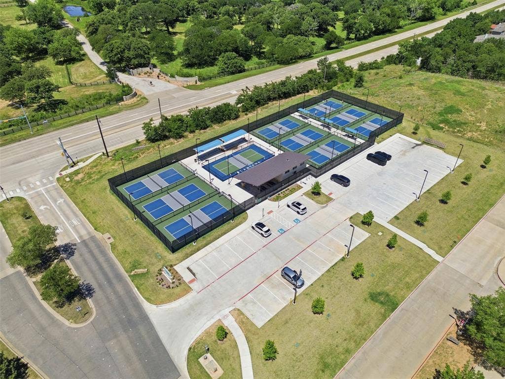 Modern recreation facility featuring multiple pickleball courts with perimeter fencing, a dedicated parking lot, and surrounding green spaces