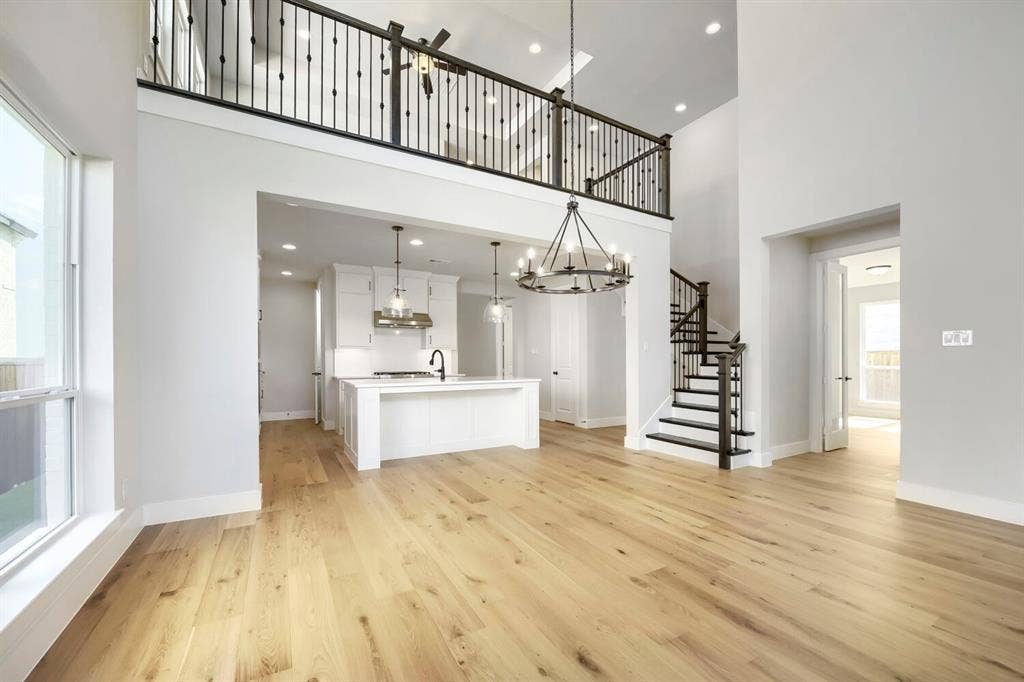 800 Blackberry Road, Haslet, TX 76052 Spacious open-concept interior featuring light wood-finish flooring, a two-story ceiling, a contemporary chandelier, a white island kitchen with pendant lighting, and a prominent staircase with dark iron balusters
