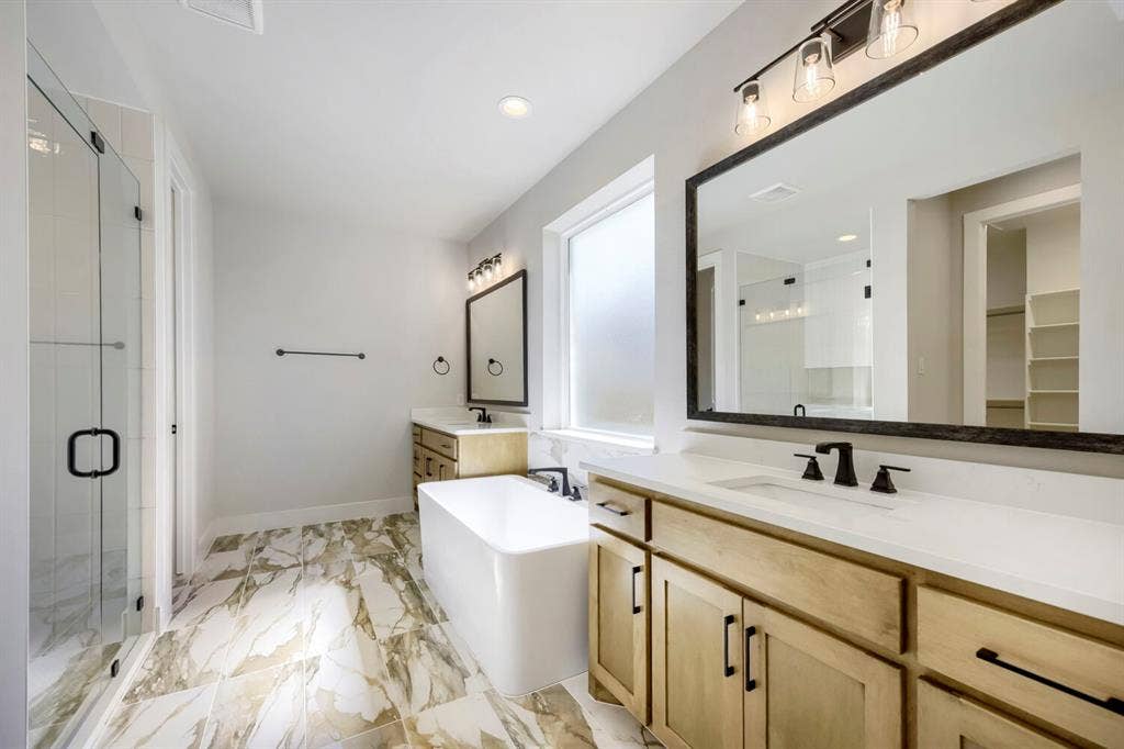 800 Blackberry Road, Haslet, TX 76052 Dual sink vanity with light wood cabinetry and stone-finish countertops, featuring a freestanding soaking tub, a frameless glass shower enclosure, and large-format tile flooring