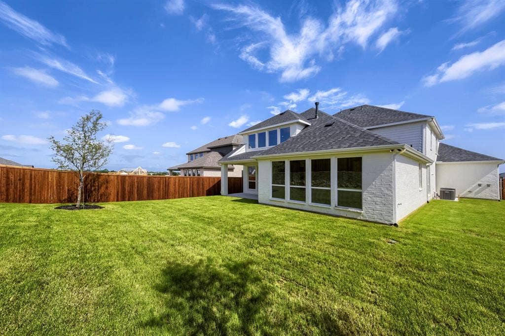 800 Blackberry Road, Haslet, TX 76052 Expansive green lawn bordering a tall privacy fence, featuring a young tree and a two-story residence with white brick and siding, a dark shingle roof, and multiple large windows