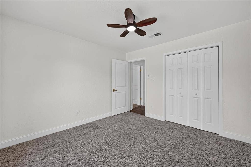 3420 Denbury Drive, Fort Worth, TX 76133 Interior room featuring neutral wall paint, gray carpeting, a dark wood-finish ceiling fan with integrated lighting, and white bi-fold closet doors