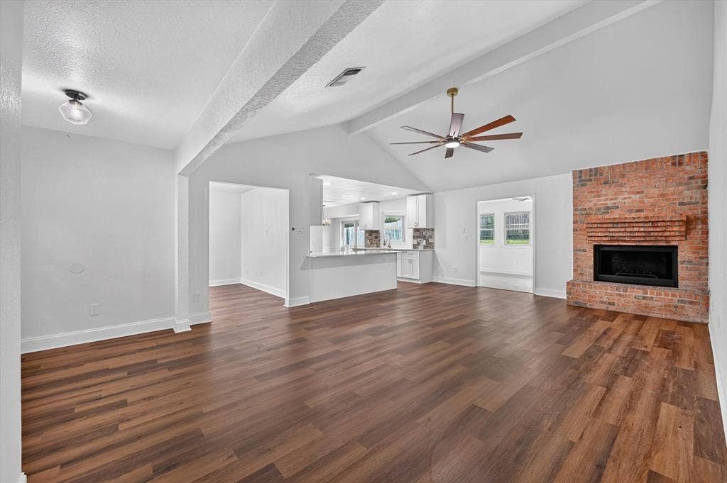 3420 Denbury Drive, Fort Worth, TX 76133 Spacious living area featuring wood-finish flooring, a brick fireplace, a vaulted ceiling, and a large ceiling fan
