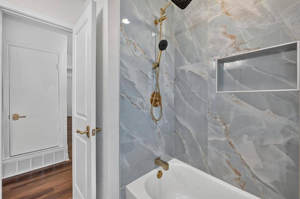 3420 Denbury Drive, Fort Worth, TX 76133 Bathroom featuring a bathtub with a gold-finish faucet and showerhead, marble-look wall tiling, and a recessed shower niche