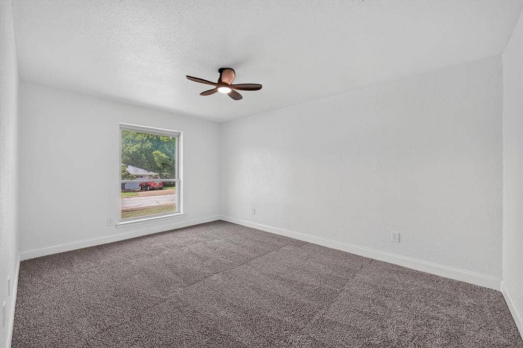 3420 Denbury Drive, Fort Worth, TX 76133 Spacious room featuring neutral carpeting, white walls, a large window, white trim, and a ceiling fan with integrated lighting