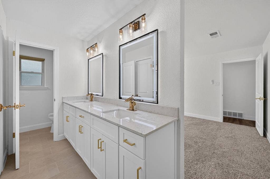 3420 Denbury Drive, Fort Worth, TX 76133 Dual vanity featuring white cabinetry, gold hardware, quartz countertops, and gold-finish faucets
