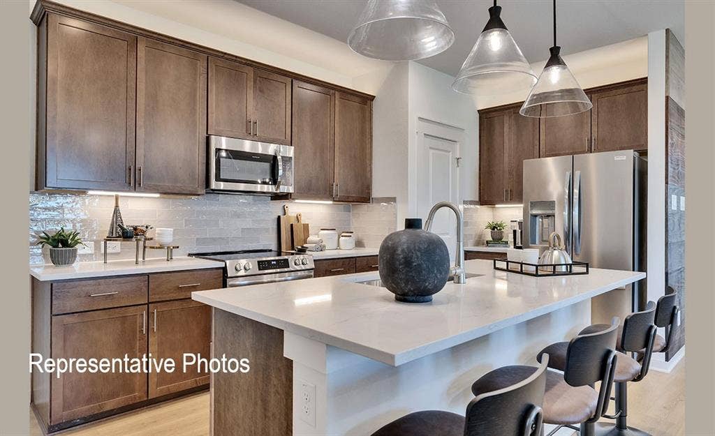 1579 Gentle Night Drive, Forney, TX 75126 Modern kitchen featuring rich wood-finish cabinetry, stainless steel appliances, a light-toned countertop, a tile backsplash, and an island with pendant lighting
