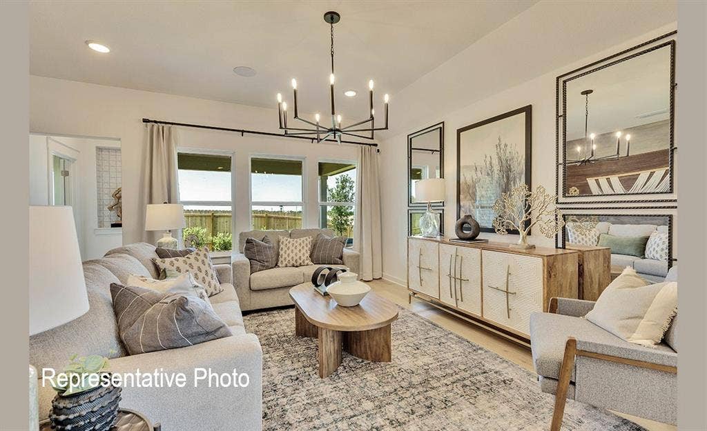 1579 Gentle Night Drive, Forney, TX 75126 Spacious living area featuring light wood-finish flooring, a contemporary chandelier, multiple large windows, and a built-in wall cabinet with integrated shelving