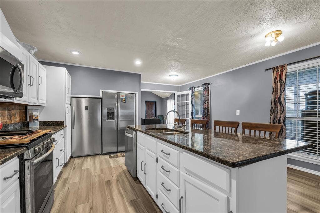 12912 Spring Valley Road, Moody, TX 76557 Kitchen featuring a central island with an undermount sink, white cabinetry, dark speckled countertops, and wood-finish flooring
