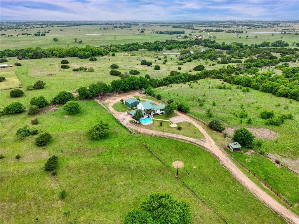 12912 Spring Valley Road, Moody, TX 76557 Expansive green acreage featuring a single-story residence with a green metal roof, a private swimming pool, a lengthy driveway, and scattered mature trees