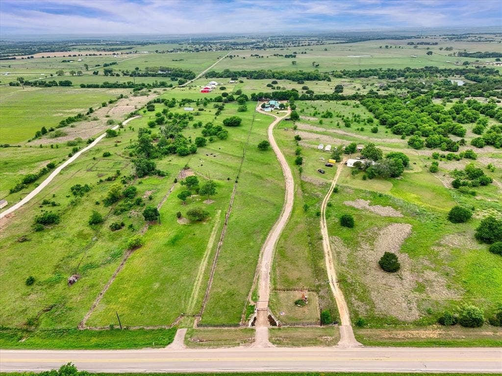 12912 Spring Valley Road, Moody, TX 76557 Expansive rural property featuring multiple access roads, verdant green fields, scattered mature trees, and a distant residential structure with outbuildings
