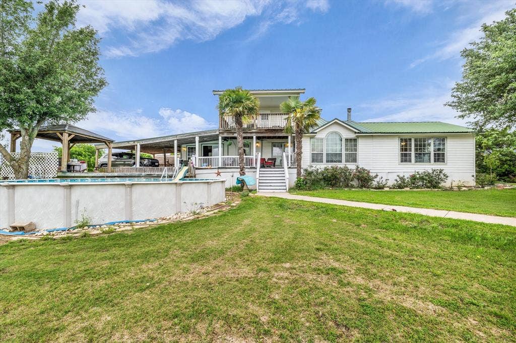 12912 Spring Valley Road, Moody, TX 76557 White-sided residence featuring a green metal roof and a two-story rear deck with stairs to the yard