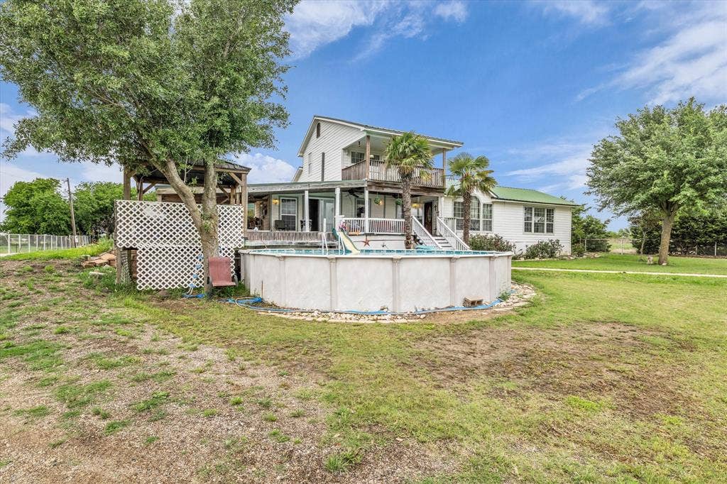 12912 Spring Valley Road, Moody, TX 76557 Two-story white exterior with a green metal roof accenting a covered porch and upper-level balcony