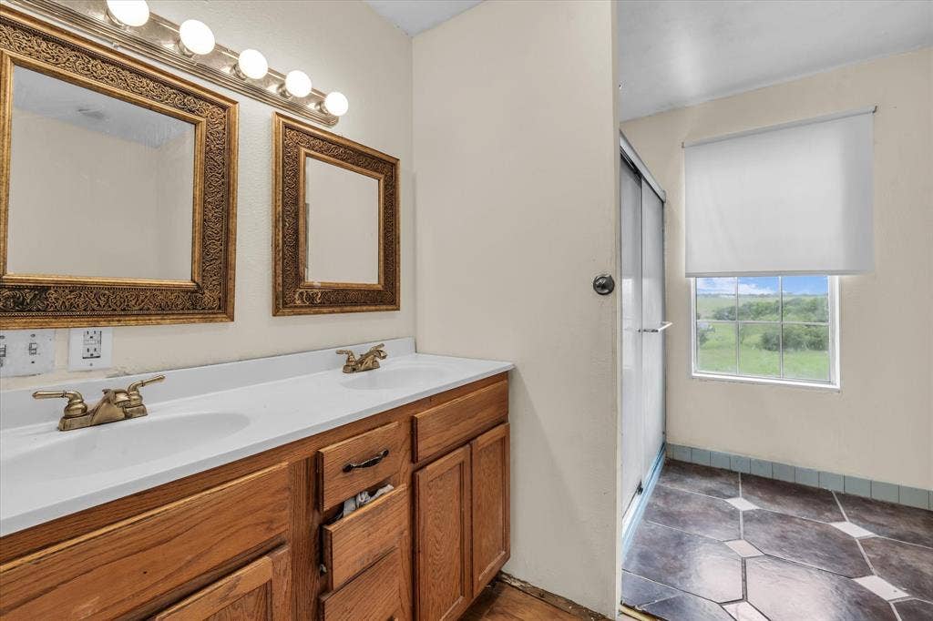12912 Spring Valley Road, Moody, TX 76557 Dual sink vanity with wood-finish cabinetry, two ornate framed mirrors, and a multi-bulb vanity light fixture