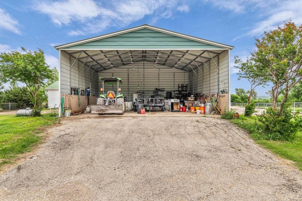12912 Spring Valley Road, Moody, TX 76557 Spacious metal-frame storage building with a green-trimmed roof, open-front design, and gravel-covered entrance