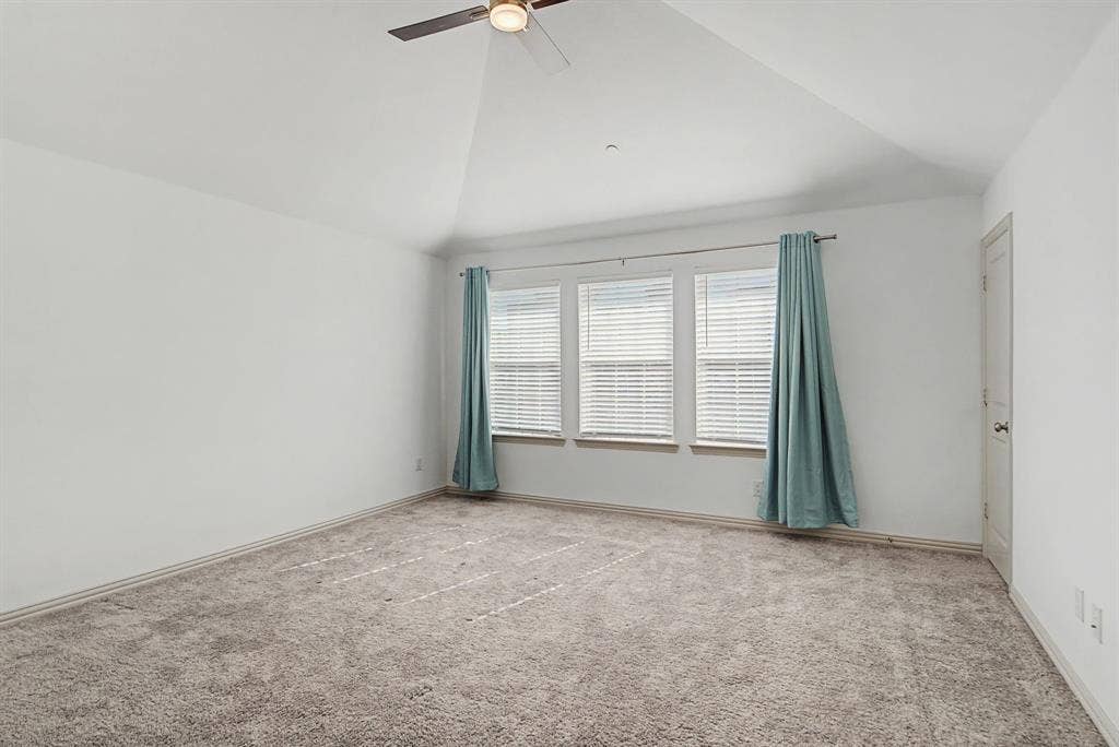 6032 Silverado Trail, McKinney, TX 75070 Spacious room featuring vaulted ceilings, plush carpeting, three windows with blinds, and a ceiling fan with integrated lighting