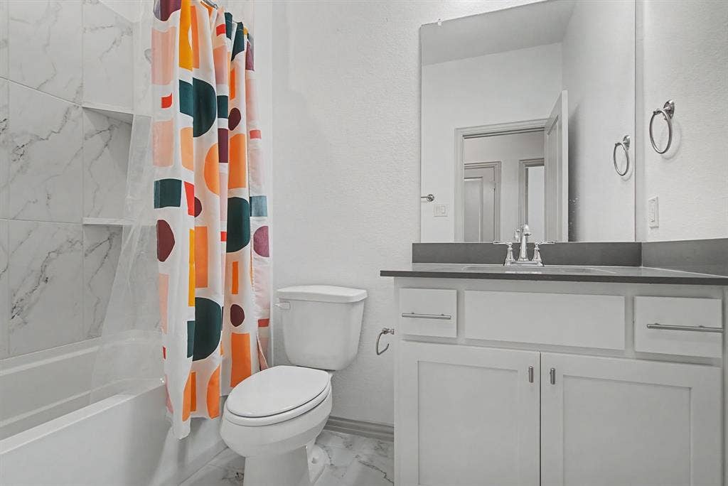 6032 Silverado Trail, McKinney, TX 75070 Bathroom featuring a white vanity with a dark countertop and undermount sink, a large wall mirror, and a toilet