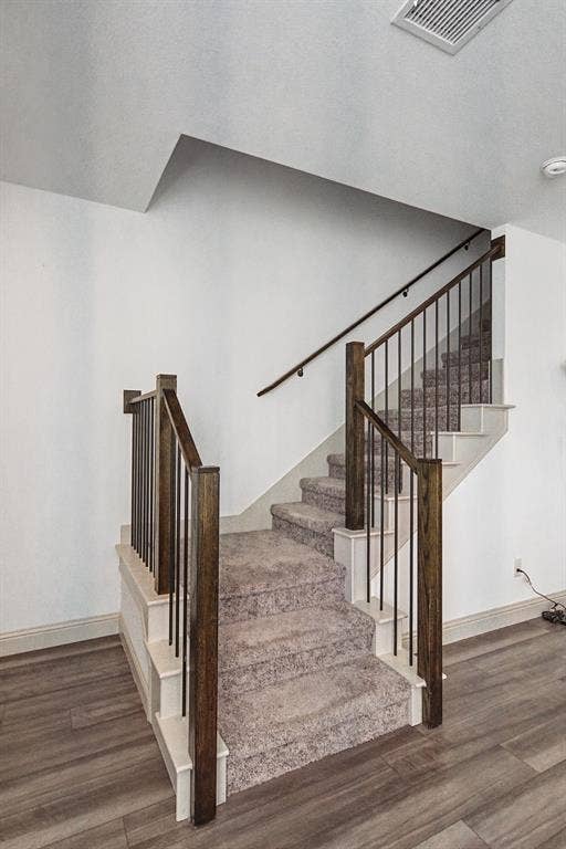 6032 Silverado Trail, McKinney, TX 75070 Staircase featuring dark wood newel posts and handrails, black iron balusters, and plush carpeted treads, complemented by wood-finish flooring