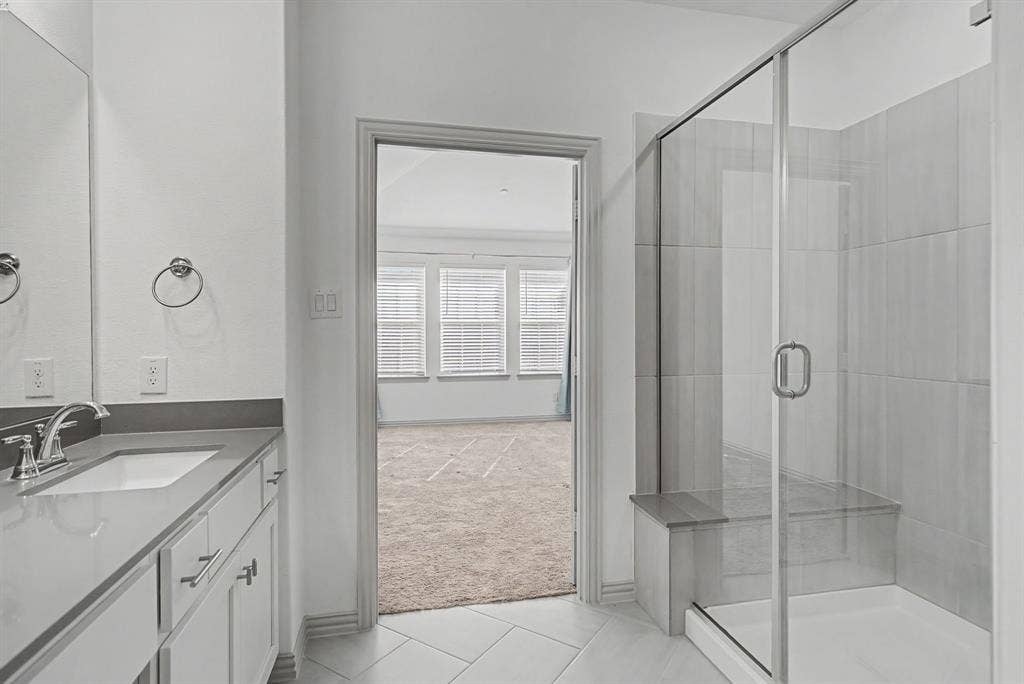 6032 Silverado Trail, McKinney, TX 75070 Bathroom featuring a single vanity with an undermount sink, a large wall mirror, and a glass-enclosed shower with a built-in bench
