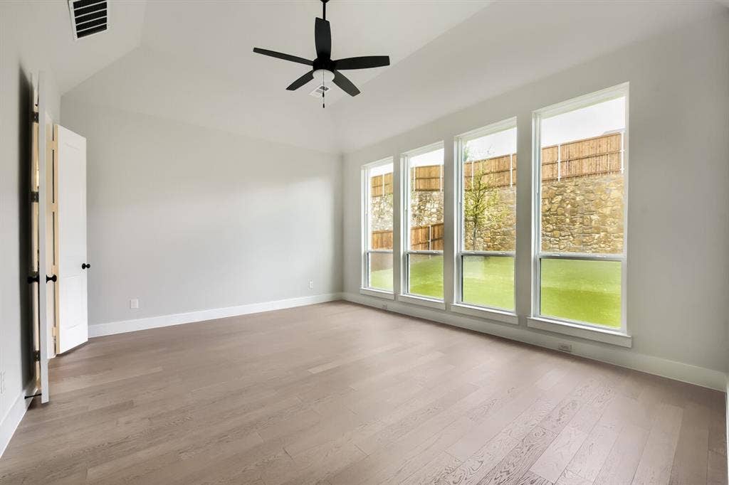 Spacious room featuring multiple tall windows, light wood-finish flooring, a vaulted ceiling, a black ceiling fan, and white trim