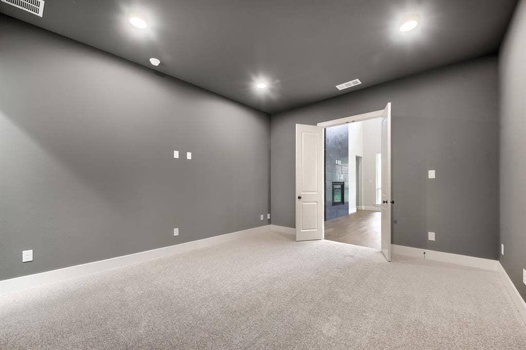 Spacious room featuring light-colored carpeting, dark gray walls, white trim, recessed lighting, and double-door entry