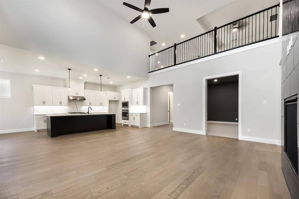 Open-concept living space featuring high vaulted ceilings with exposed beams, wood-finish flooring, and a modern kitchen